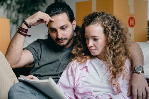 Focused male and female in casual wear sitting near boxes and looking through notebook thoughtfully while moving house