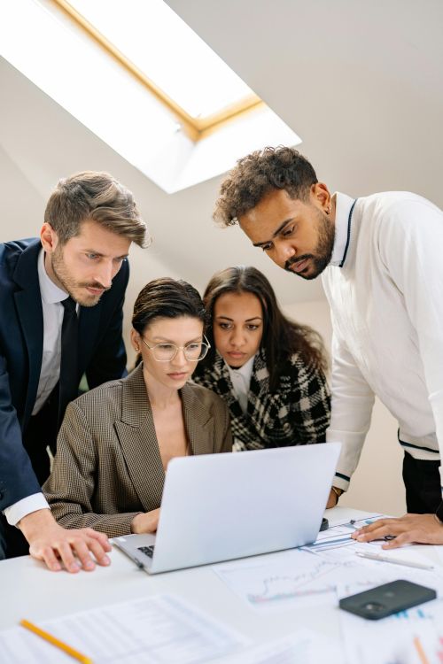 A group of diverse professionals working together on a laptop in a contemporary office space.